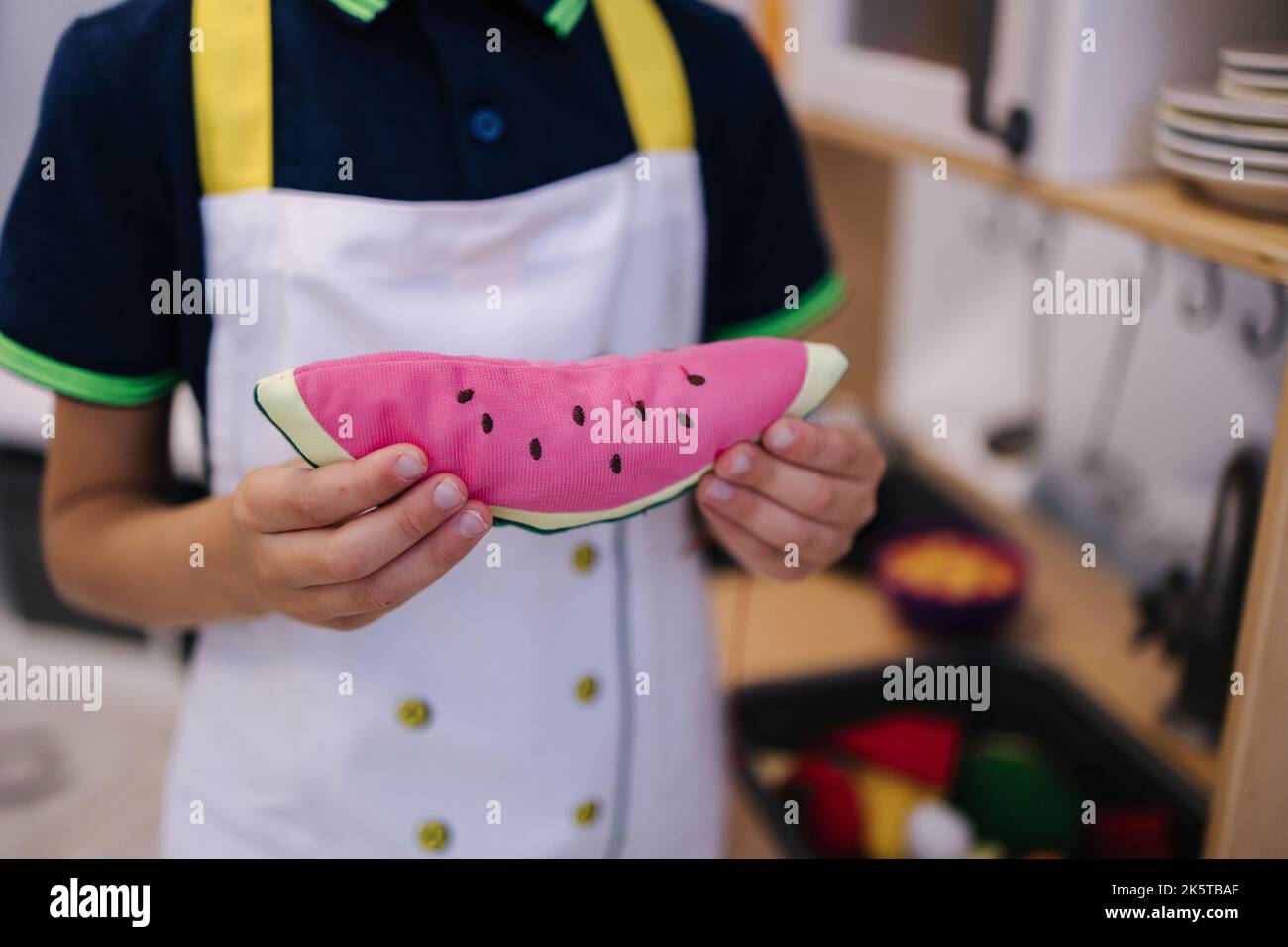 Close up of little boy playing on toy kitchen and hold soft toy in the form of a watermelon Stock Photo