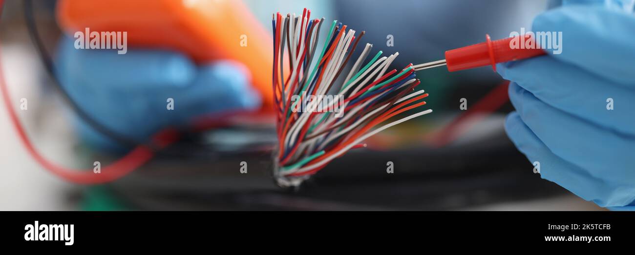Hands with a voltmeter check colored wires in the cable, blurry Stock Photo
