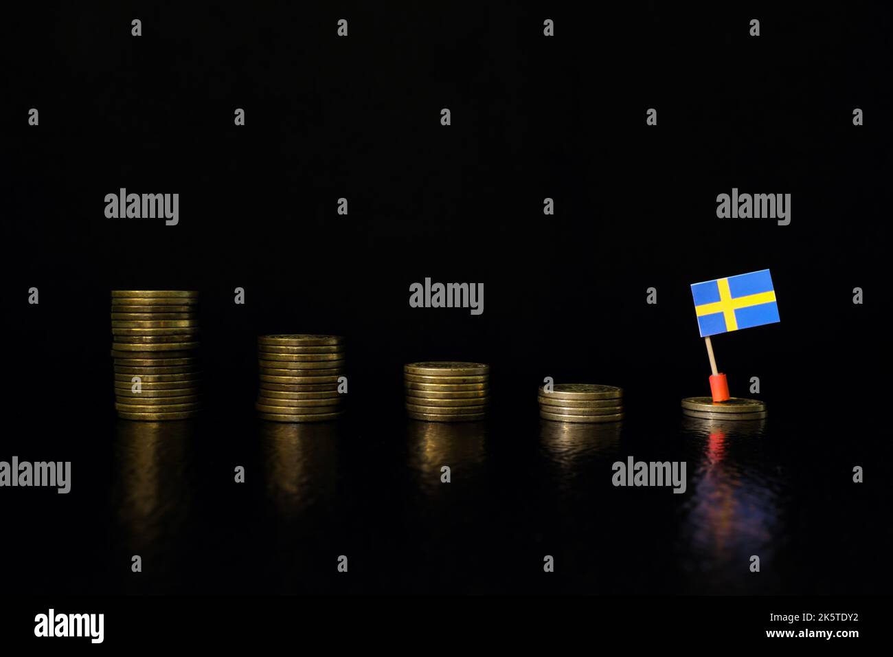 Sweden economic recession, financial crisis and currency depreciation concept. Swedish flag in decreasing stack of coins in dark black background. Stock Photo