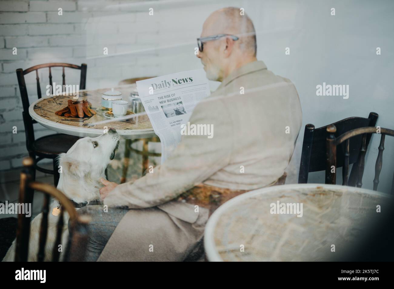 Happy senior man sitting in cafeteria with his dog and reading newspaper. Stock Photo