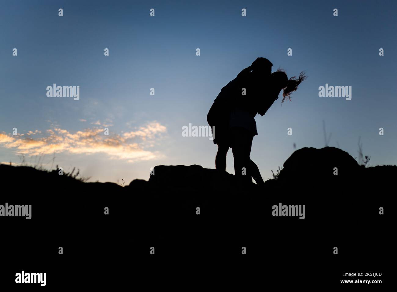 a silhouette of a romantic couple kissing on the background of blue sky ...