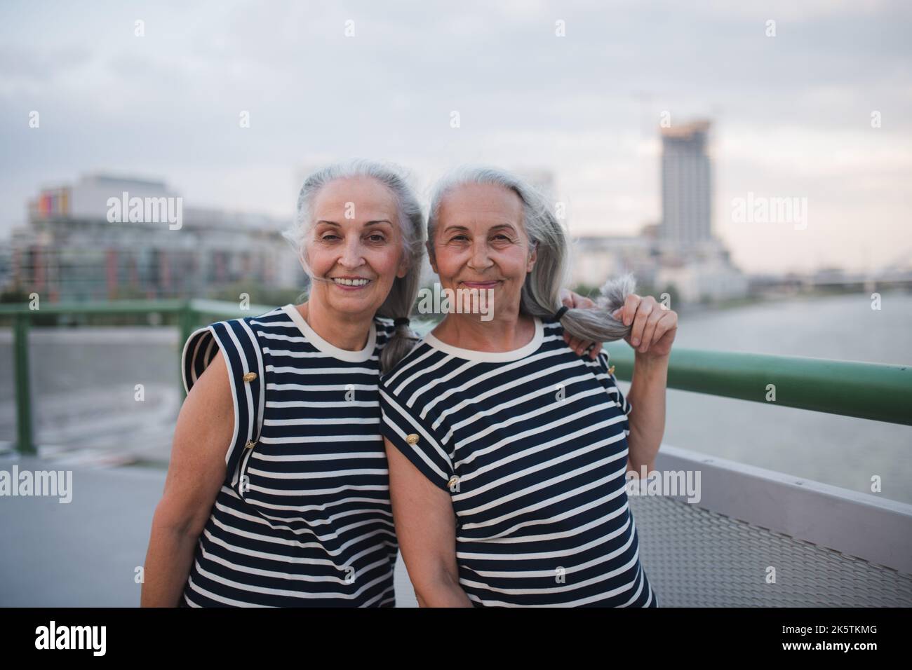 Portrait of happy seniors women, twins in same clothes, walking on city ...
