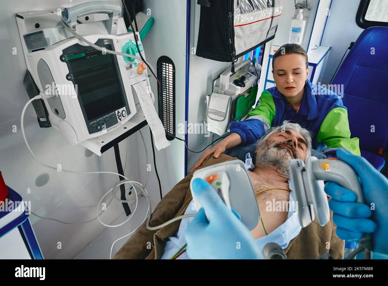First aid in ambulance. Paramedic with defibrillator pads before CPR for casualty man inside