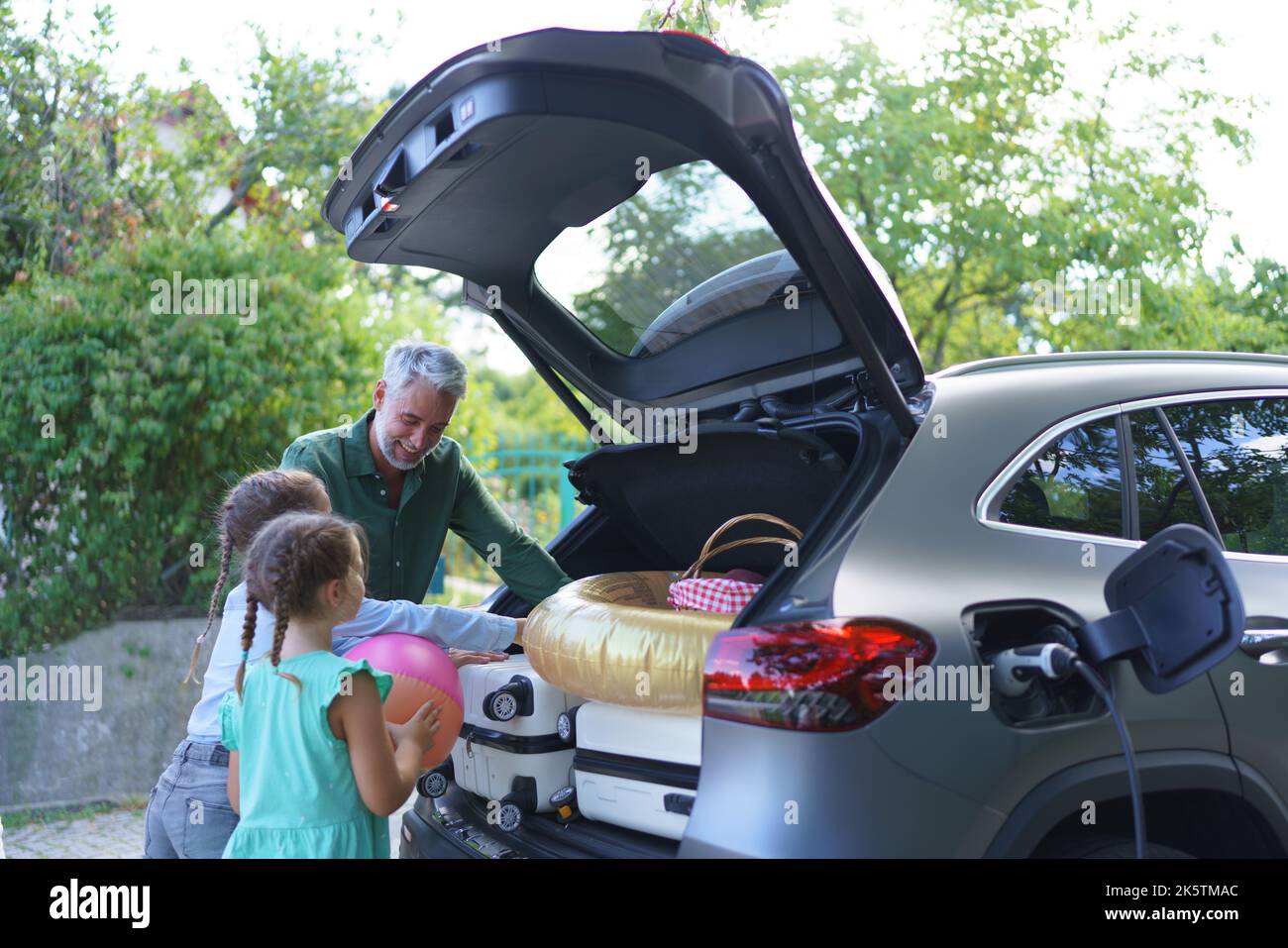 Family with little children loading car and waiting for charging car before going on picnic. Stock Photo