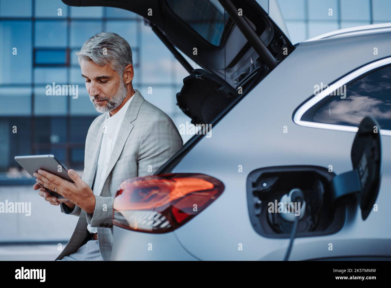 Businessman using tablet while charging car at electric vehicle