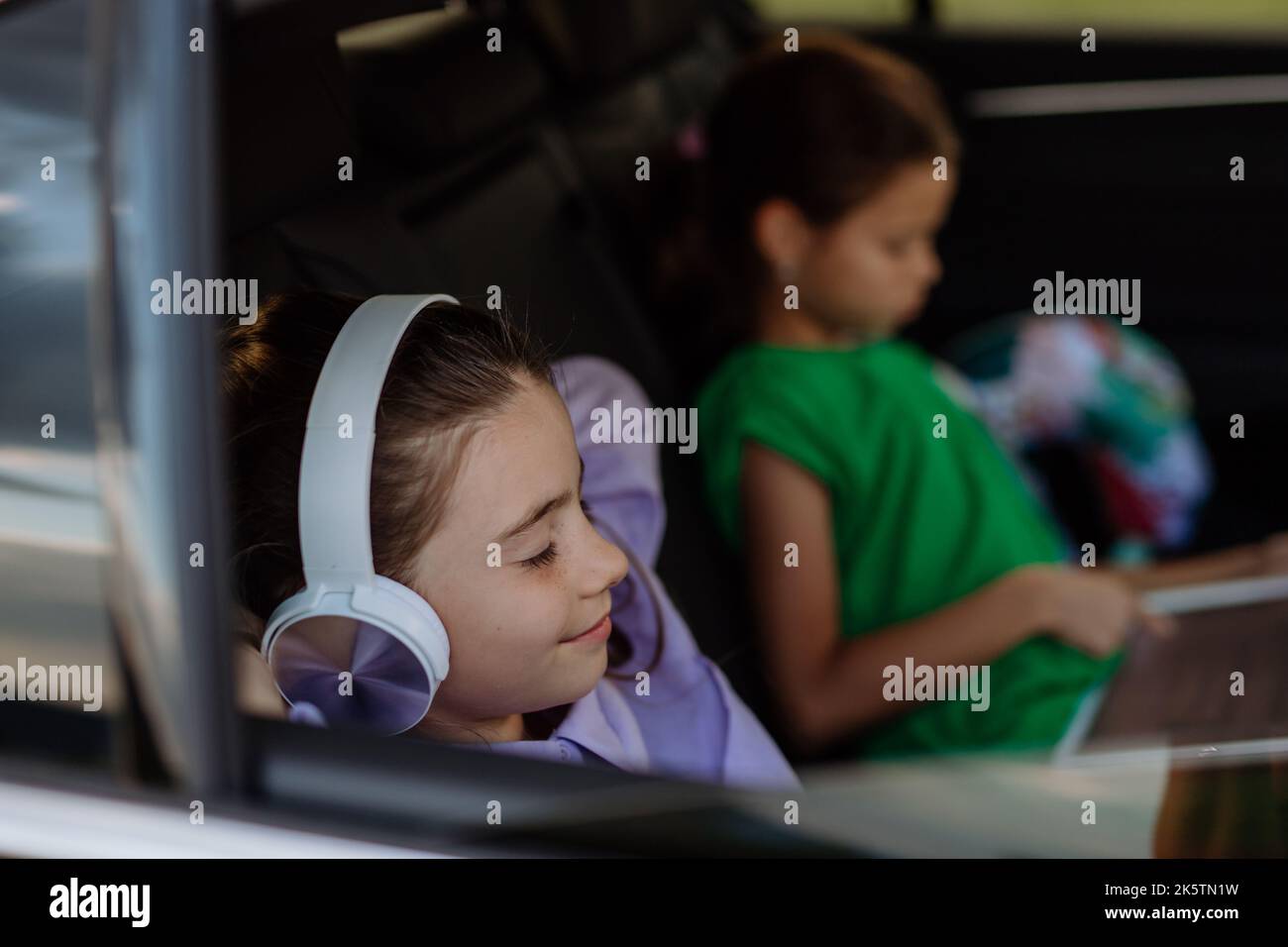 Little sisters sitting in car, listening to music and waiting for a car trip. Stock Photo