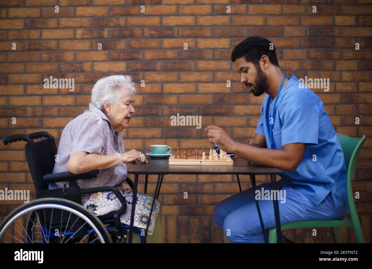 Caregiver playing chess and drinking coffe with his client outdoor at cafe. Stock Photo