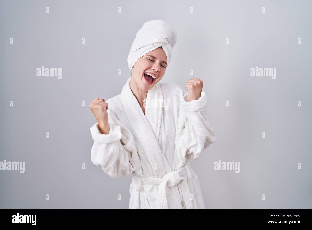 Blonde caucasian woman wearing bathrobe celebrating surprised and