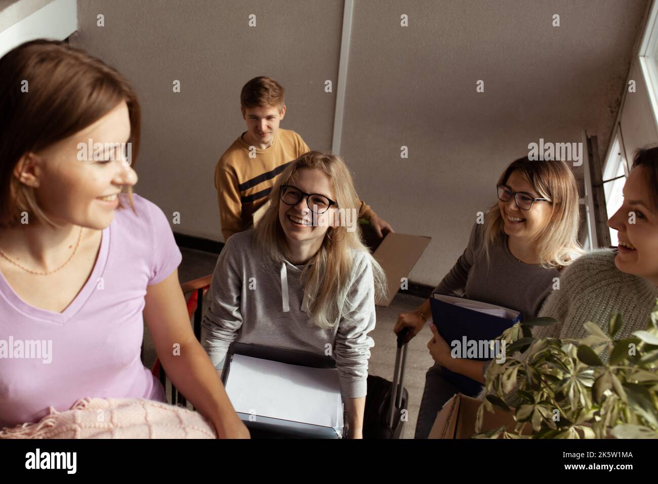 Smiling, glad, foretaste anticipating students carry luggage on the stairs, talking and joking while passage relocation Stock Photo