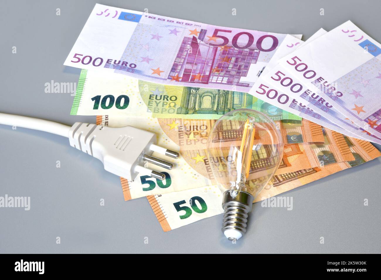 Electric plug, light bulb and euro money banknotes over grey background