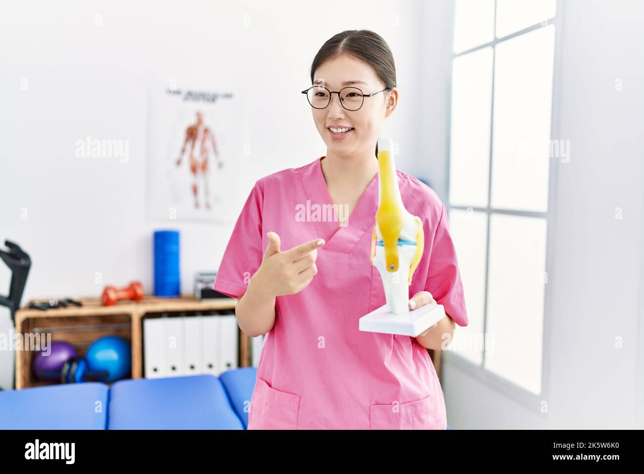 Young asian woman holding anatomical knee model at physiotherapy clinic