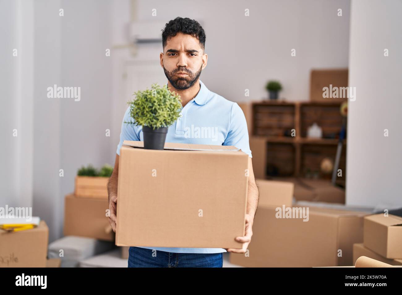 Hispanic man with beard moving to a new home holding box puffing cheeks ...