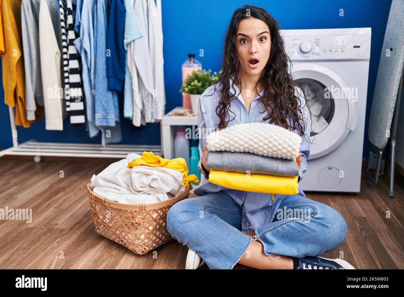 Young woman holding clean laundry in shock face, looking
