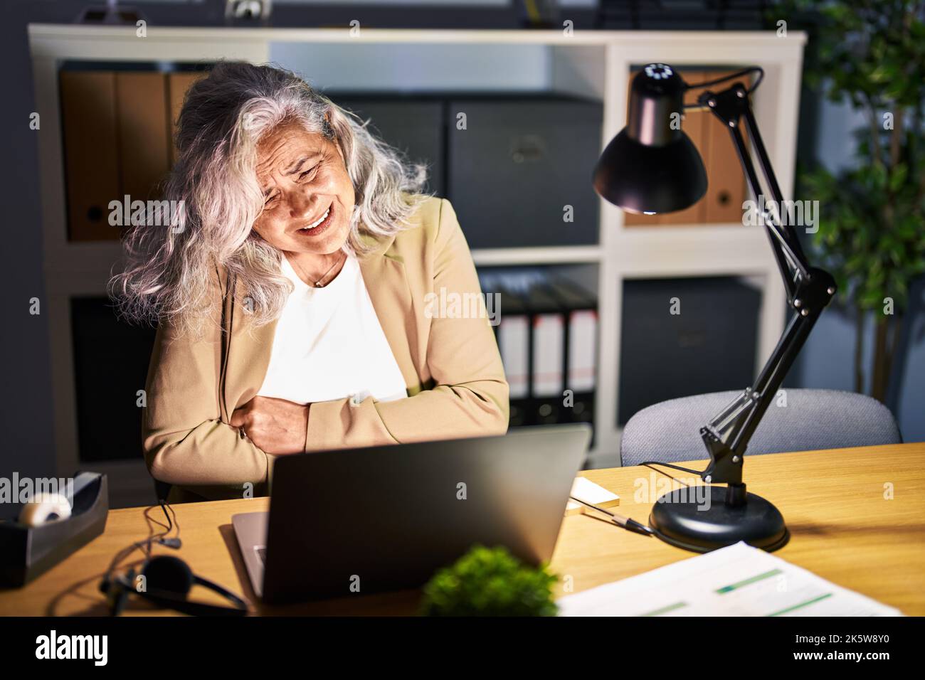 Middle age woman with grey hair working using computer laptop late at