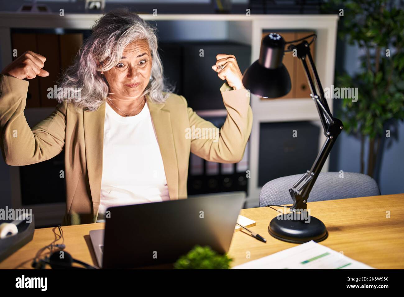 Middle age woman with grey hair working using computer laptop late at ...