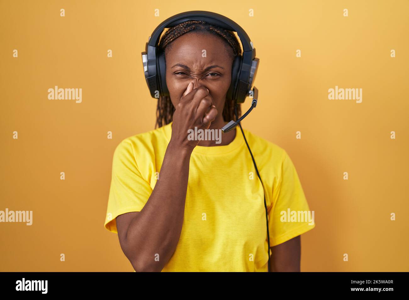African american woman listening to music using headphones smelling something stinky and
