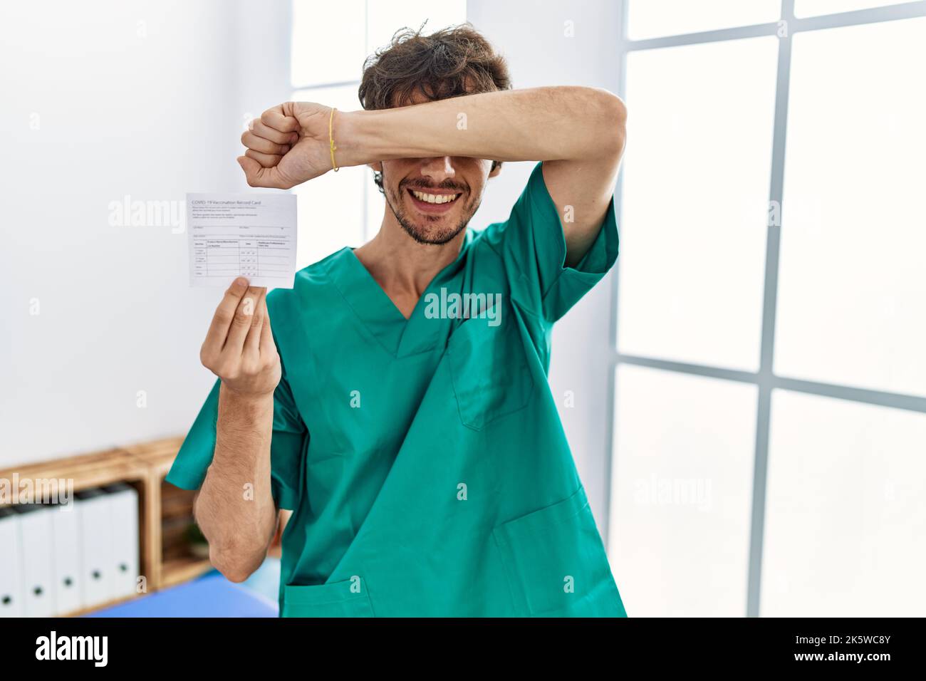 Young hispanic doctor man holding covid record card smiling cheerful ...
