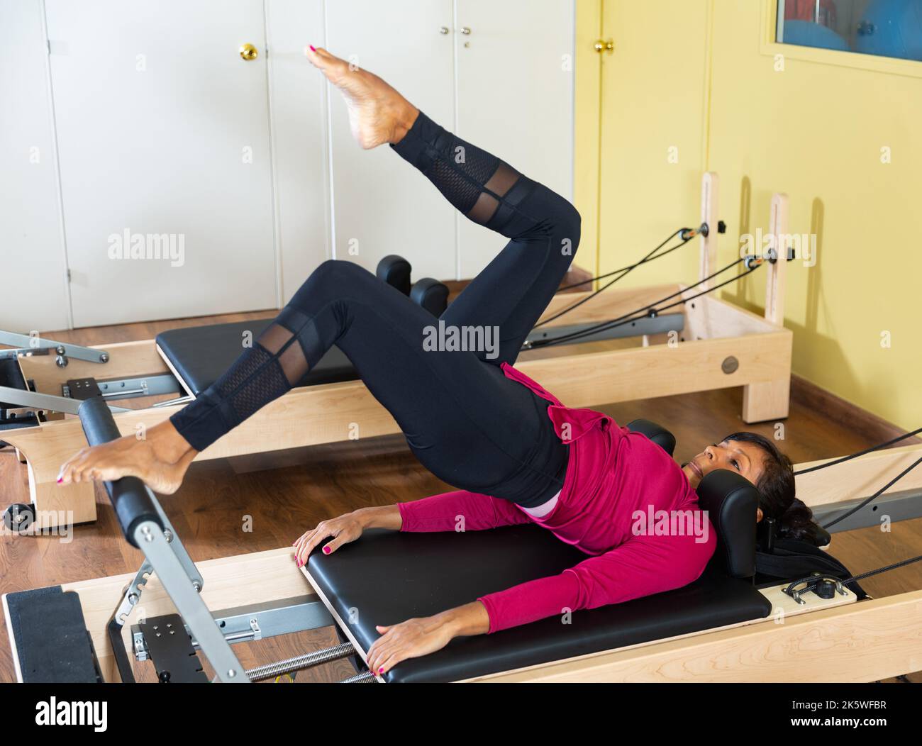 Sporty adult Latina doing stretching exercises on pilates reformer