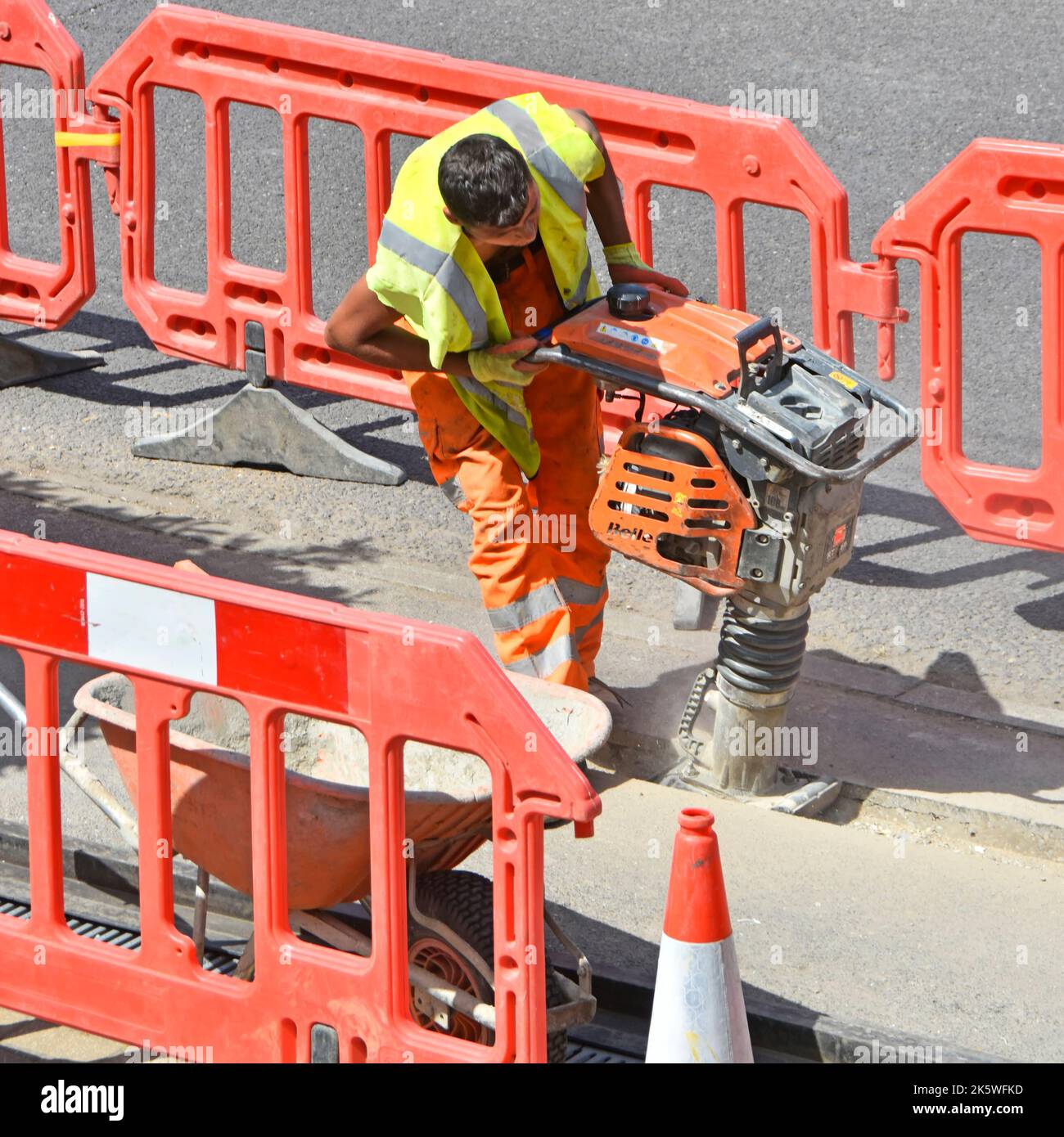 Man working whacker vibrating compactor tool on pavement road works underground broadband cable trench backfill wearing high visibility clothes UK Stock Photo