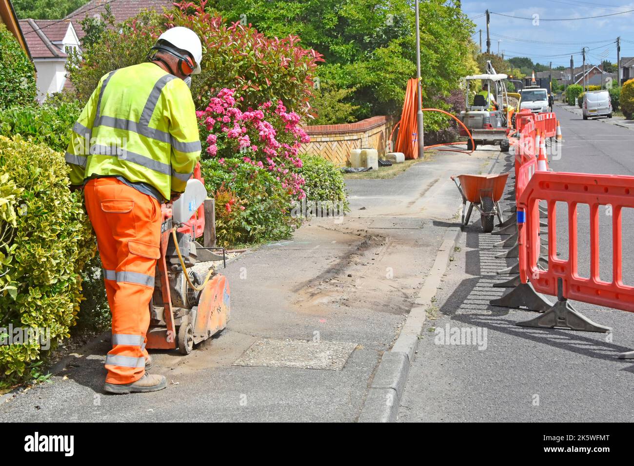 Health & safety kit worn by road works construction site worker using disc saw cutting machine new underground broadband cable infrastructure site UK Stock Photo