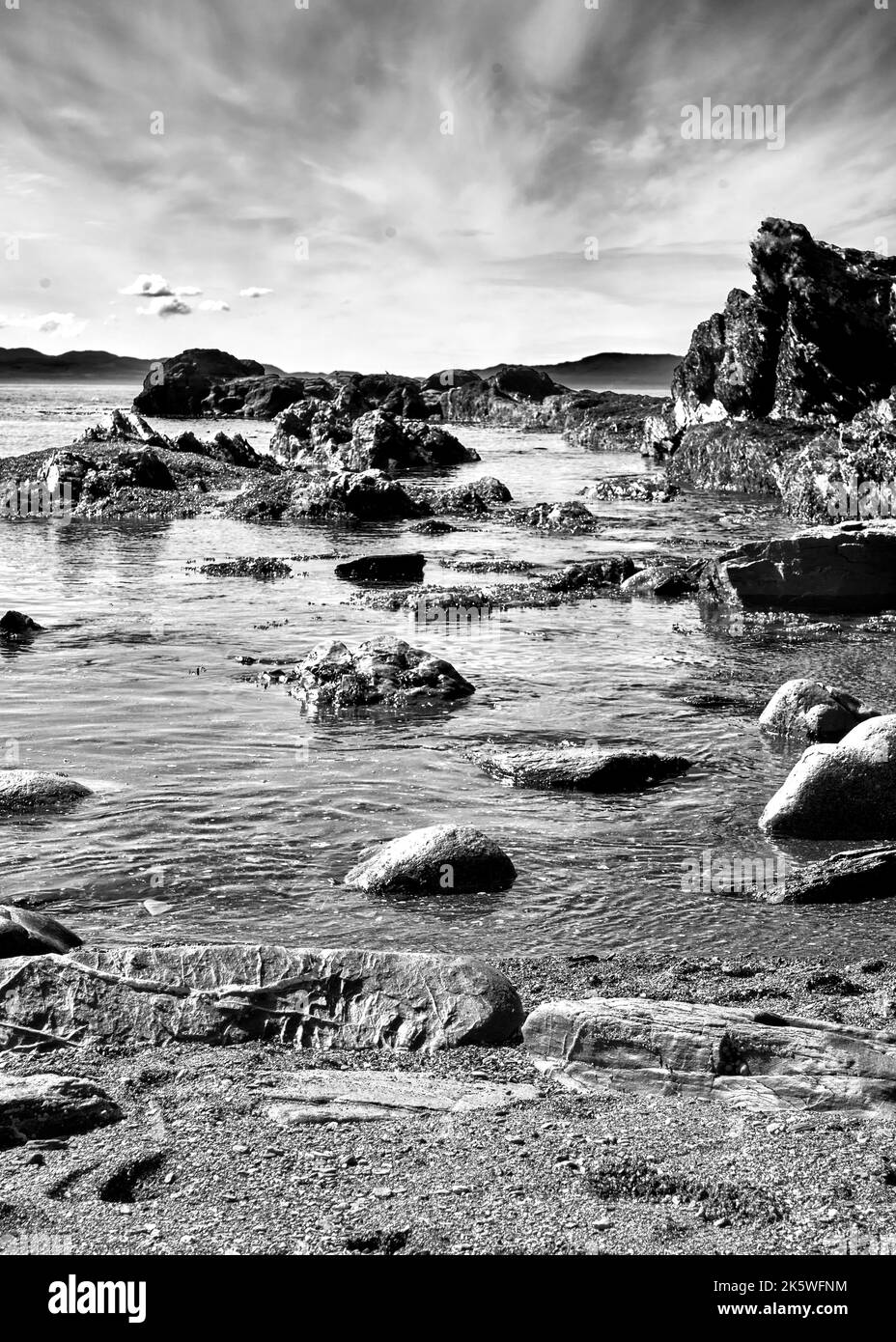 Black and white image showcases the jagged dark ocean rocks beneath a ...