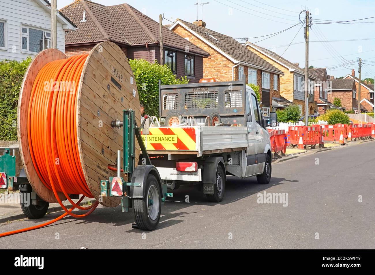 Cable drum trailer contractors pick up truck beside pavement trench working on Fibre Optic Broadband road works in village residential street Essex UK Stock Photo