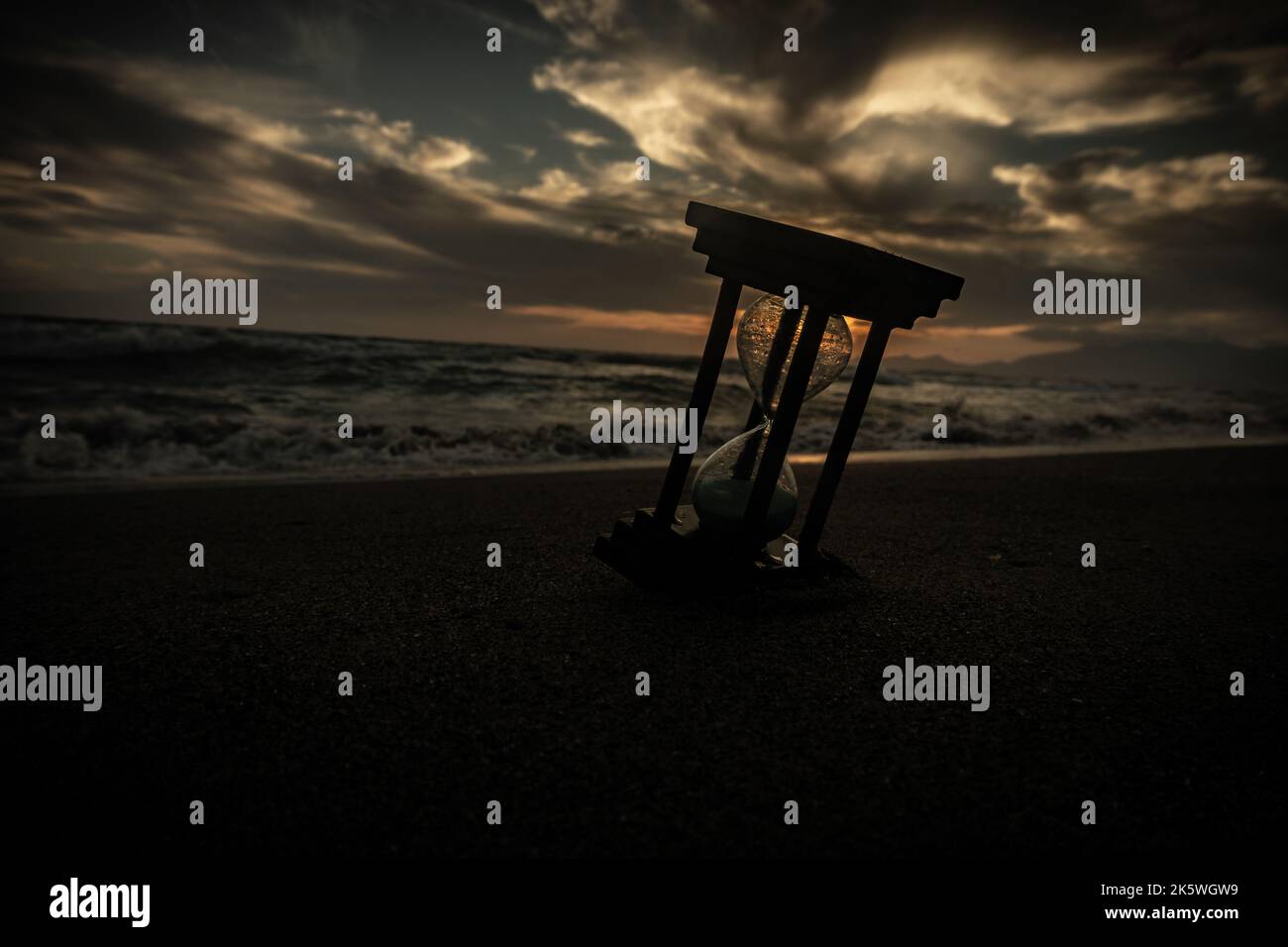 An hourglass sand on the beach at sunset, with a sea and sky as a background. Stock Photo