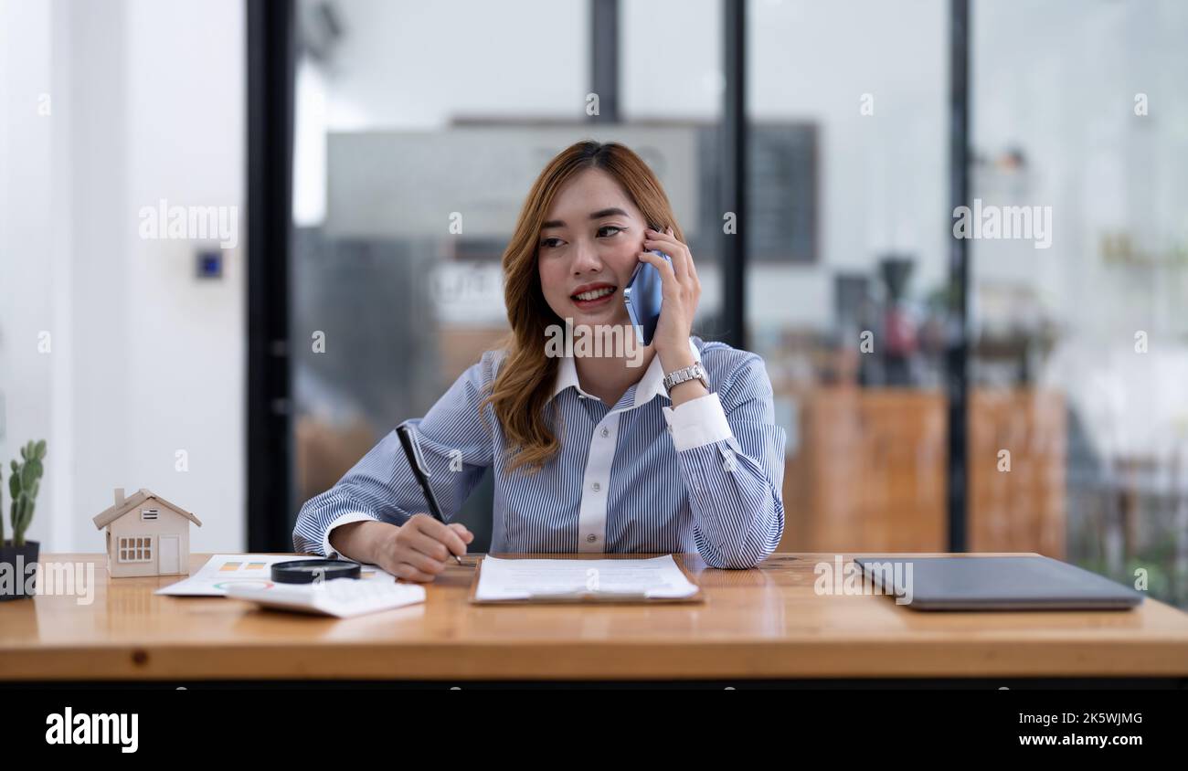 Smiling asian businesswoman, lawyer, real estate agent, banker or consultant making cell phone call to client at office. Stock Photo