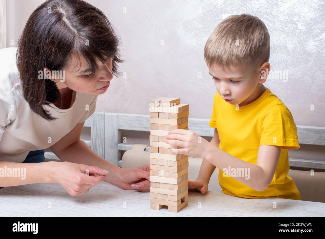 Interested happy little blond boy playing board game with middle aged mature mom taking bricks from wooden tower keeping balance having fun together a Stock Photo