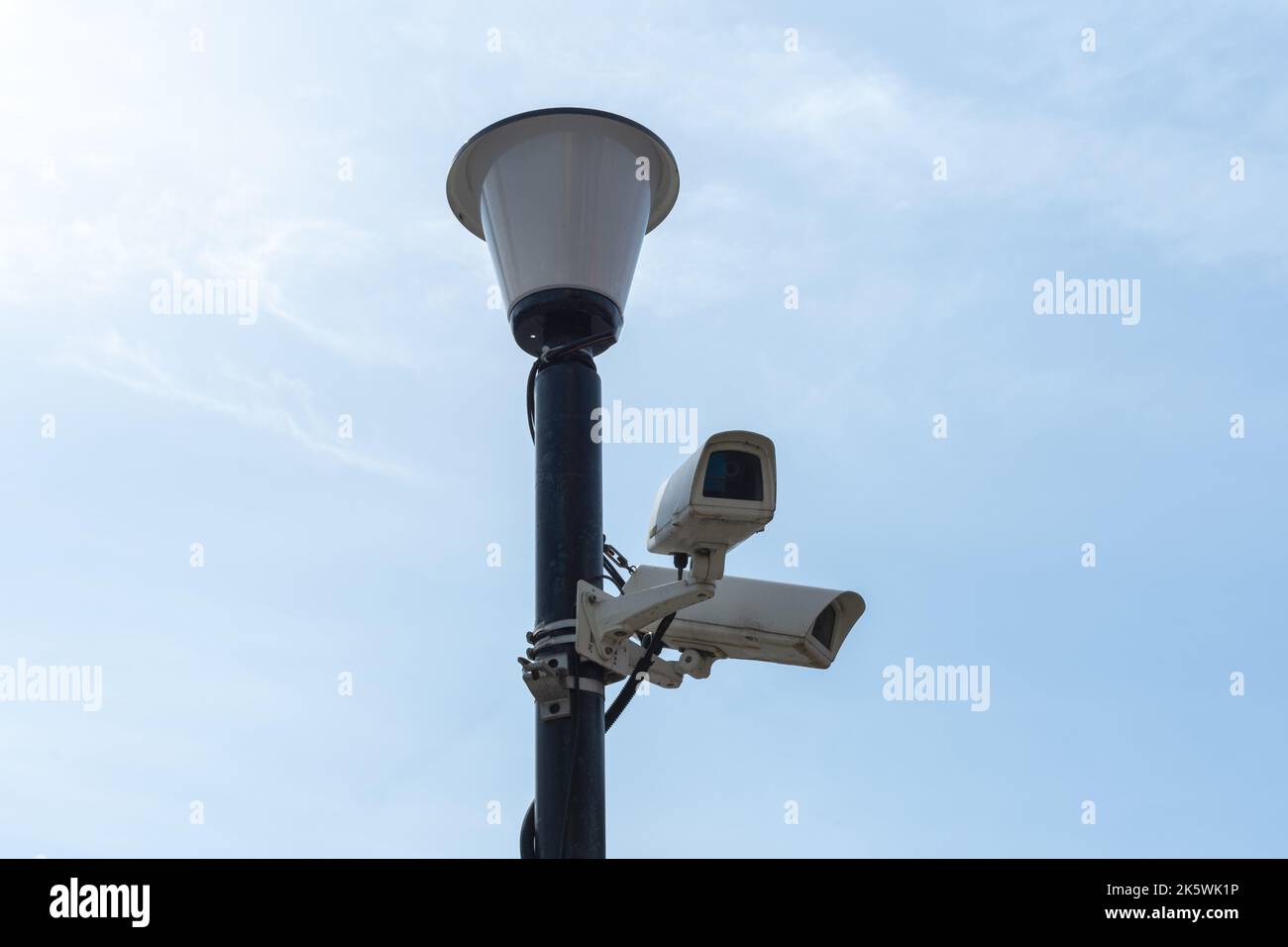 Surveillance cameras mounted on a lamp post against a blue sky. security cctv camera. Security in the city. Hidden filming of what is happening. Moder Stock Photo