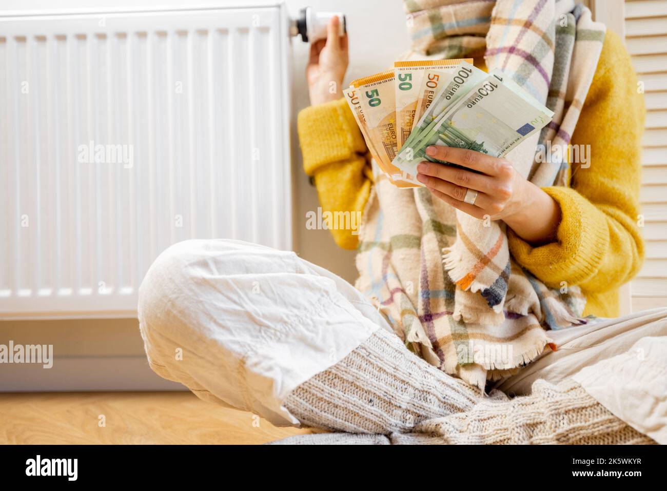 Warmly dressed woman counting money near radiator Stock Photo