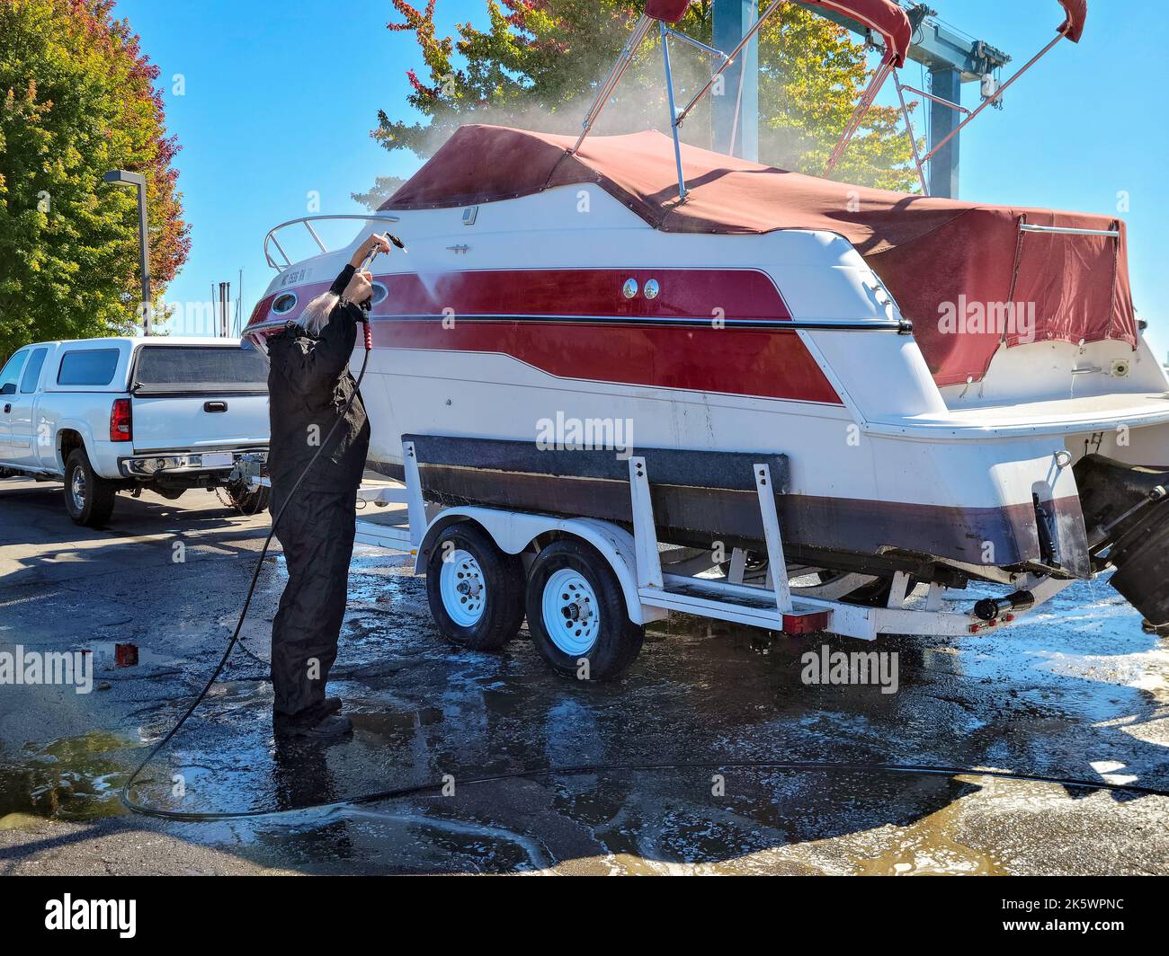 Man using a pressure washer to clean power boat on a trailer Stock Photo