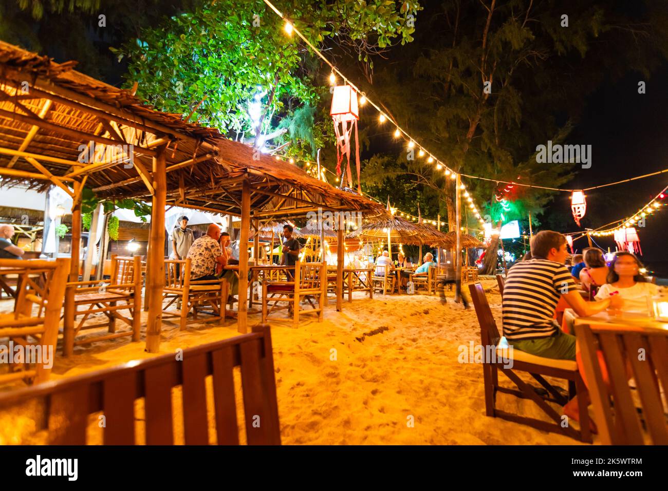 Koh Lanta, Thailand - 10.11.2019: View of small beach bar at night, at Ko Lanta island, Thailand. Chairs and tables are placed on sand. Many lightbulb Stock Photo