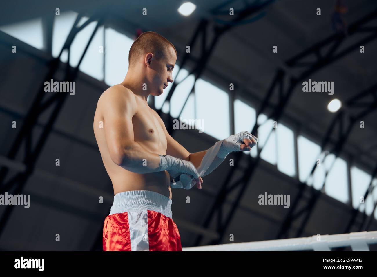 Male boxer wrapping his hands before fighting at sports gym, indoors. Closeup of young athlete