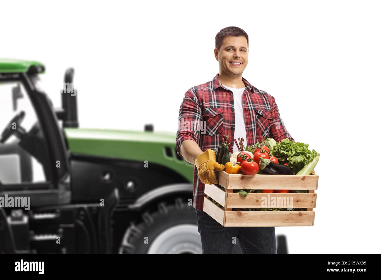 Farmer with a crate of vegetables standing in front of a tractor isolated on white background Stock Photo