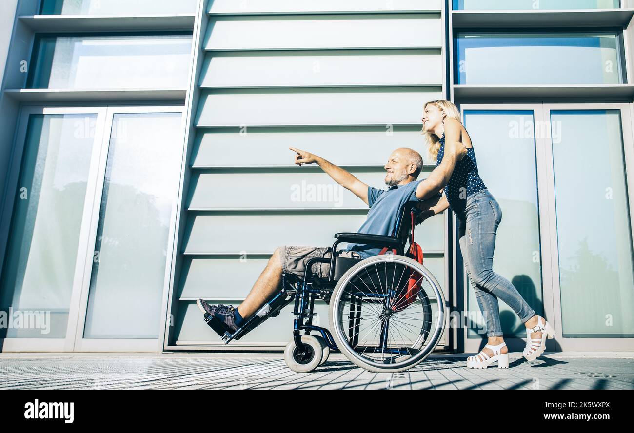 Happy couple with disabled man hanging around at urban city background - Relationship concept within disability issues with guy on wheelchair and youn Stock Photo