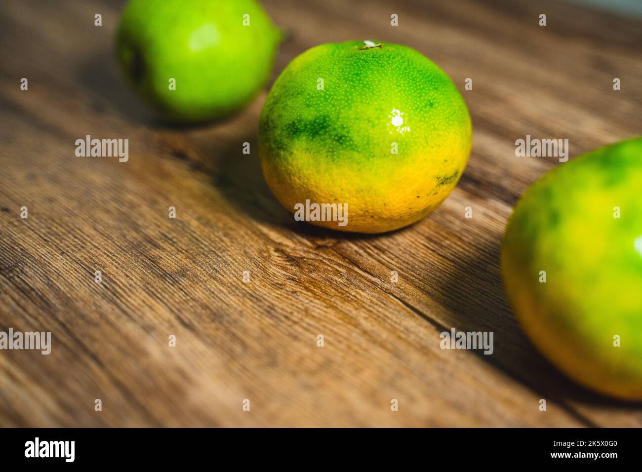 A selective focus of an orange on a wooden table with a green pear in the background. Stock Photo