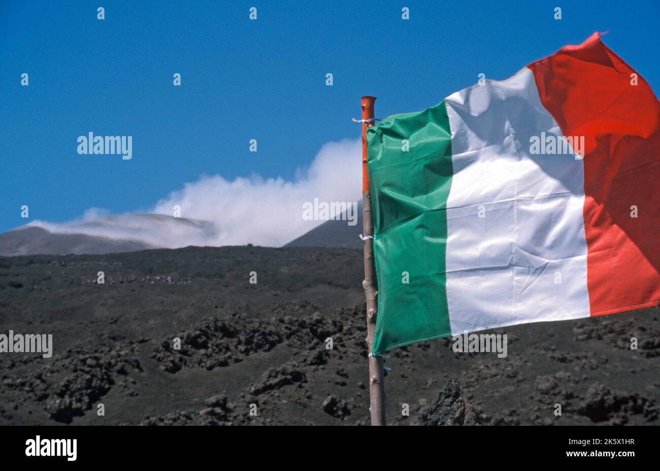 italienische Flagge (Tricolore) unter dem Aetna-Gipfel, Rauch am Aetna-Gipfel - italian flag on lava under smoking summit of Etna volcano Stock Photo