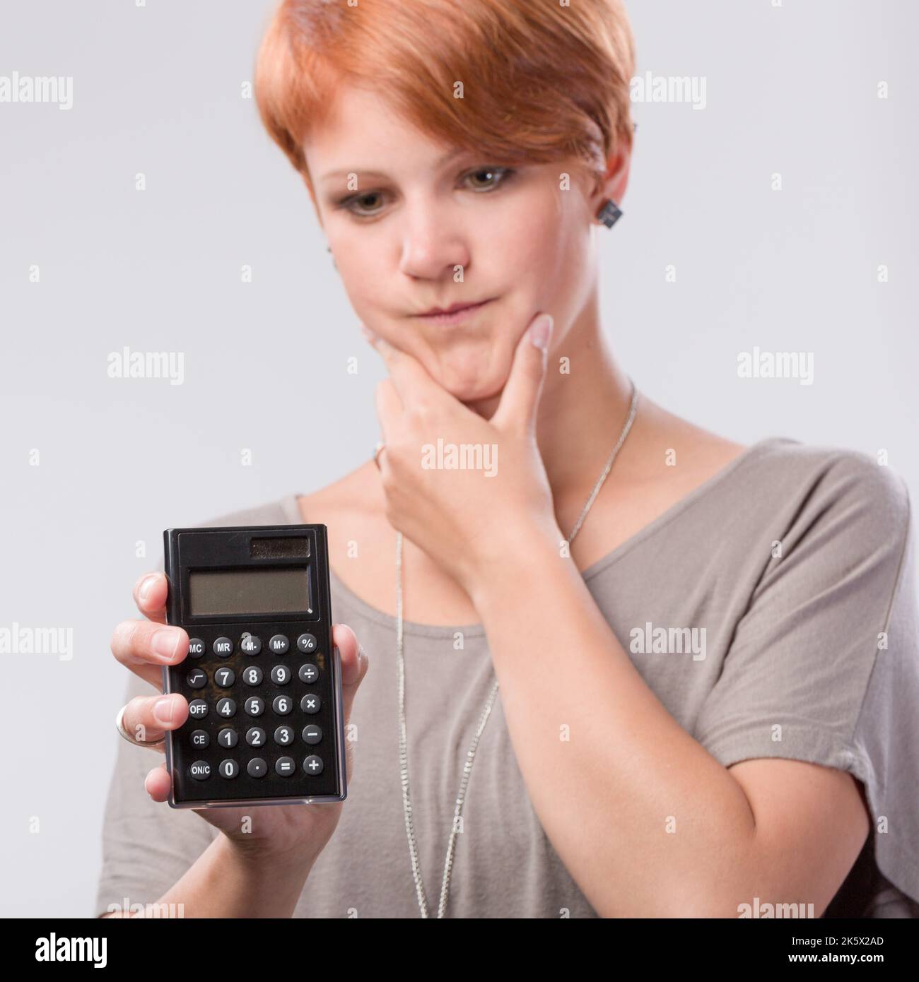 young red haired woman is worried about numbers on a calculator Stock Photo