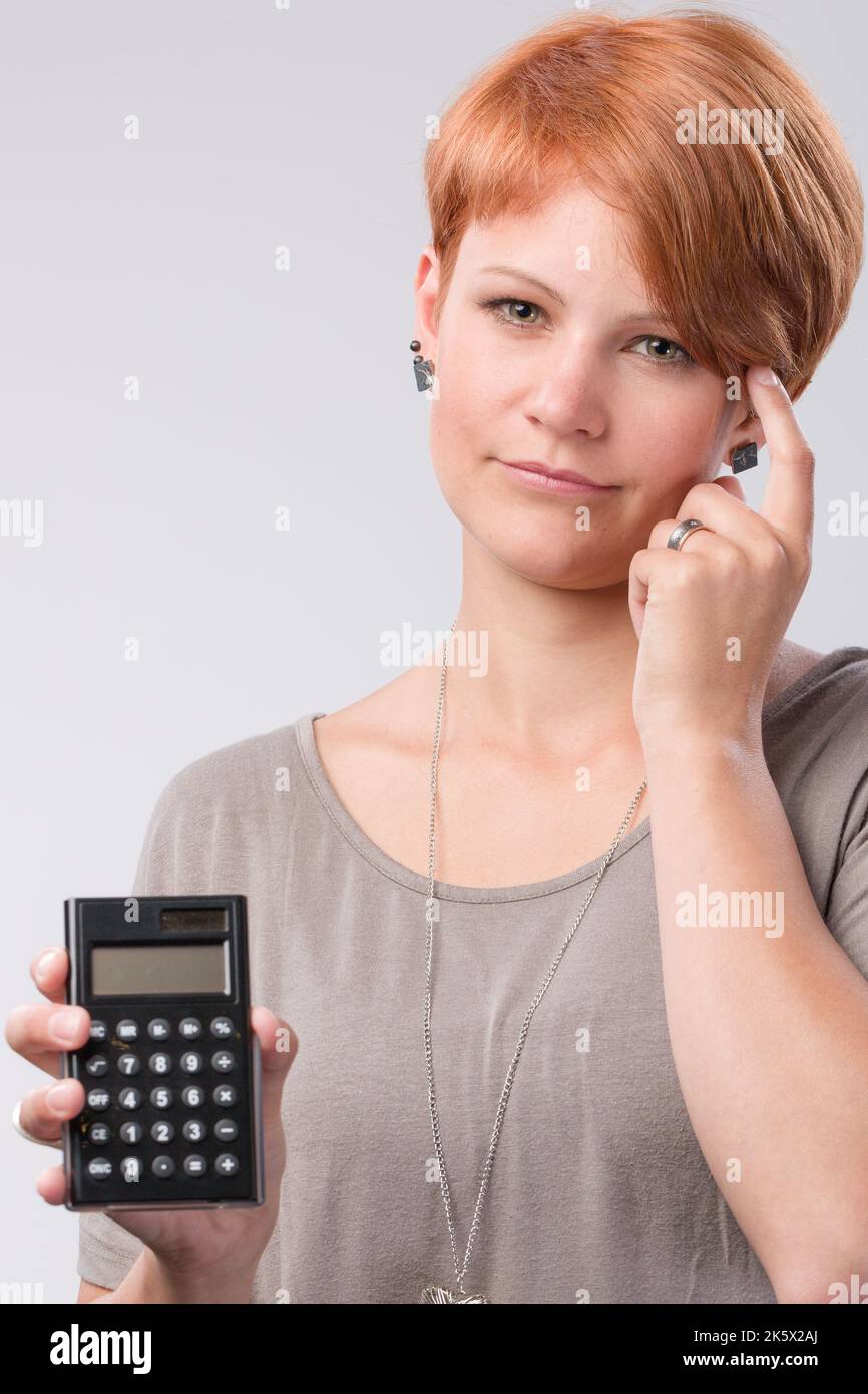 young red haired woman is worried about numbers on a calculator Stock Photo