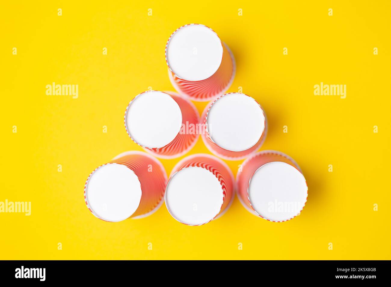 A pyramid of striped red paper cups, on a yellow background. Flat lay ...