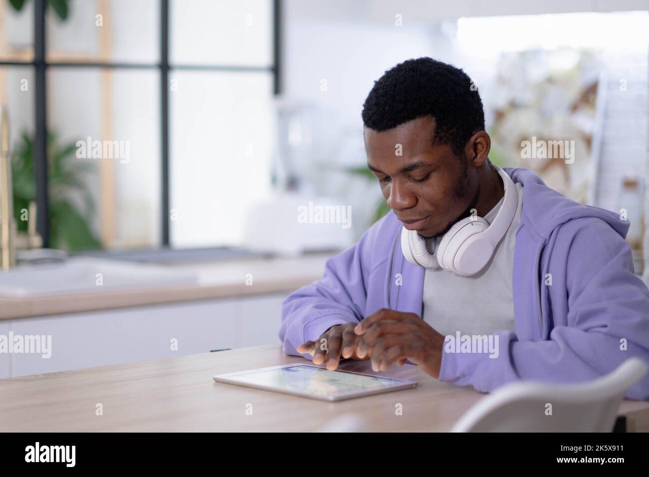 Black man using digital tablet on kitchen at home, working office work remotely typing text, African american freelancer using notepad computer Stock Photo