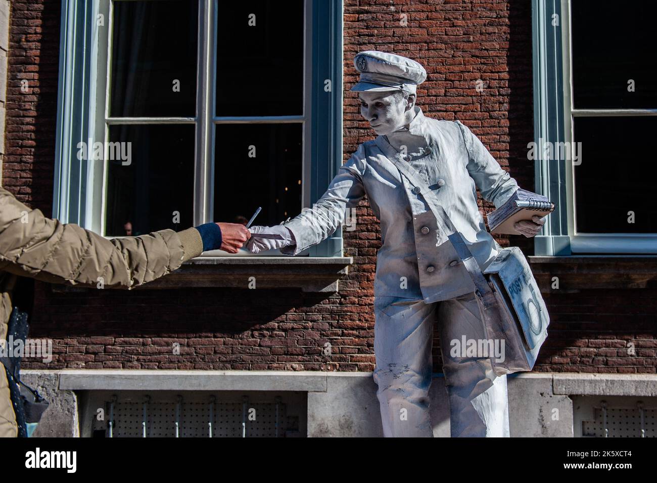 A female living statue dressed like a postman is seen interacting with