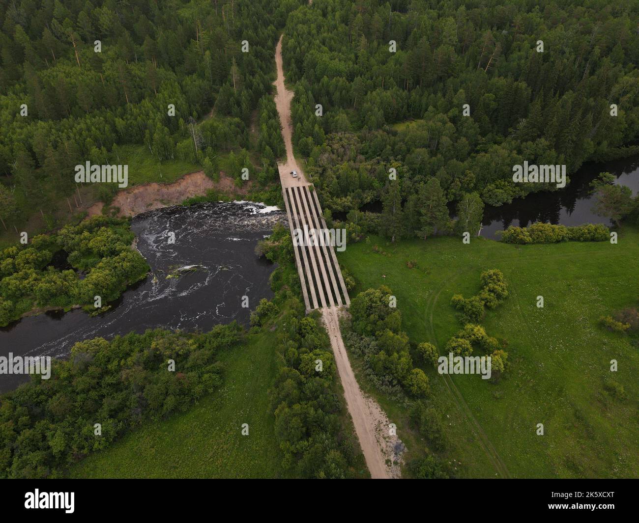 An aerial view of a green field with trees and river with a bridge ...