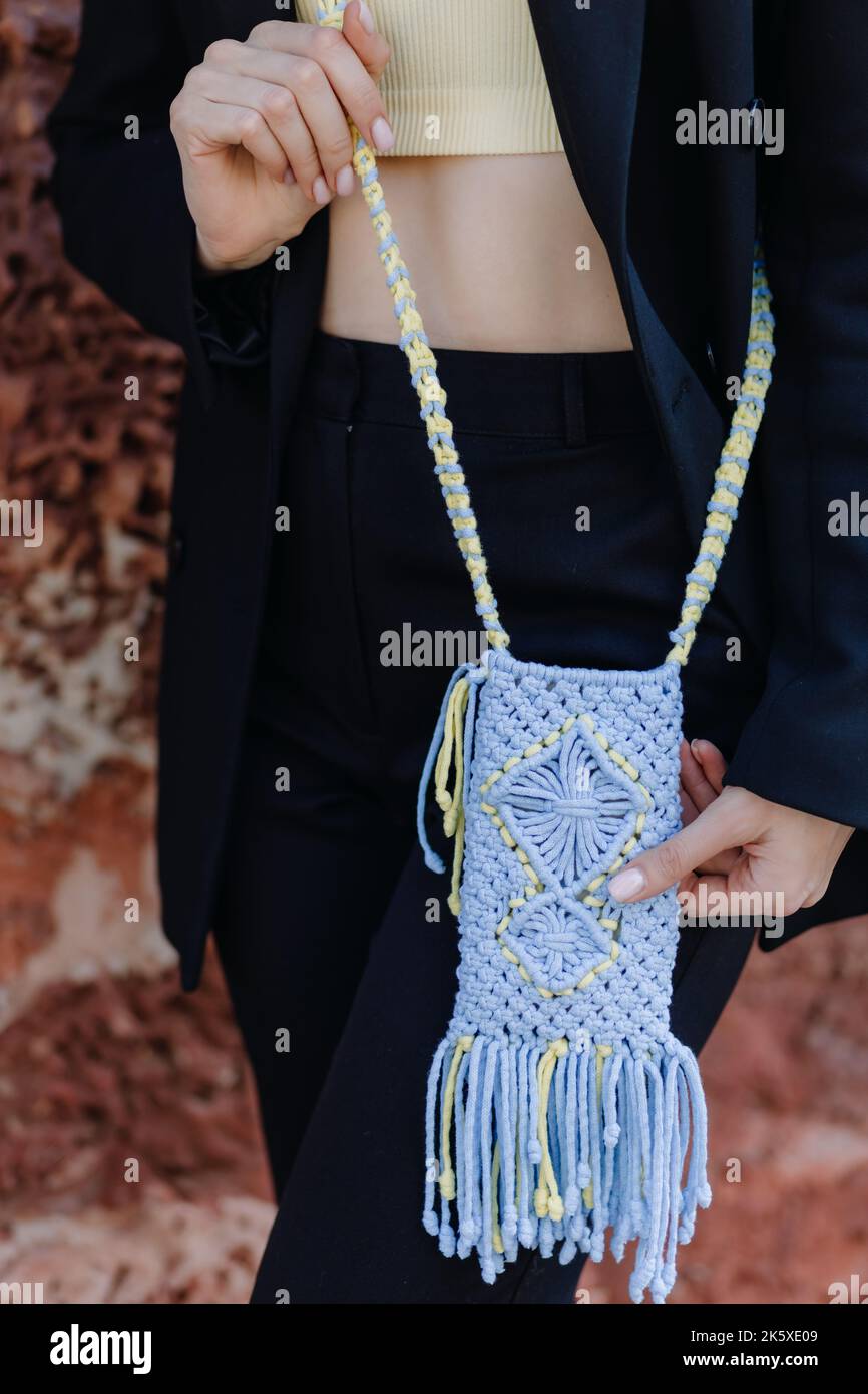 A woman in a black suit holds a knitted phone case in Ukrainian colors with macrame on the street. Close up Stock Photo