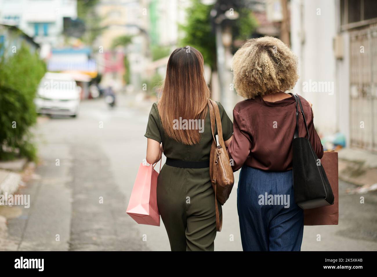 Rear view of young women with purchases walking together along the city ...