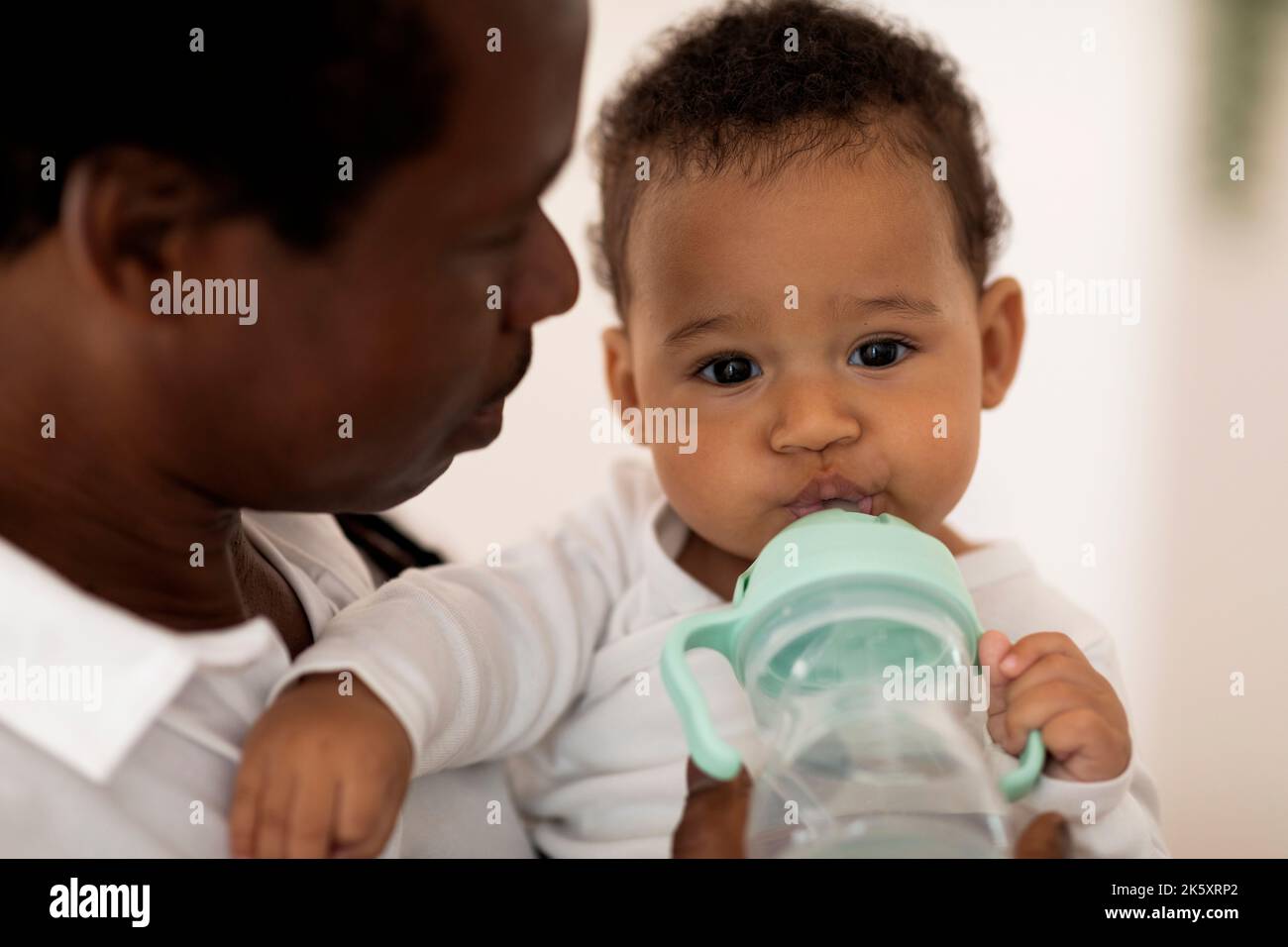 Adorable Black Baby Drinking Water From Bottle While Relaxing In Father