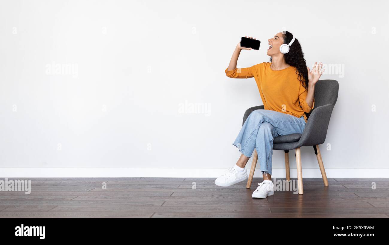 Happy woman singing on white, using smartphone and headphones Stock Photo