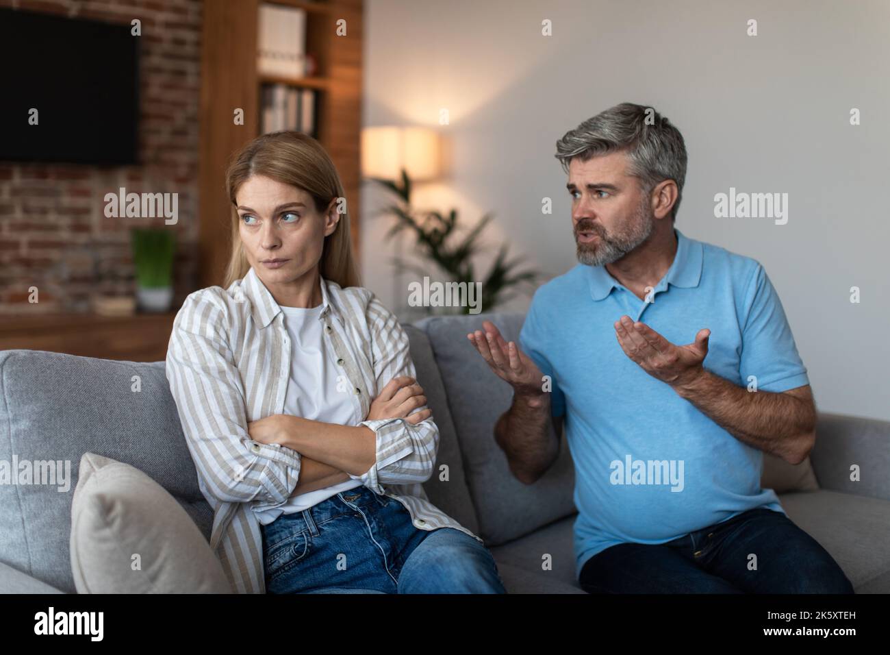 Sad offended middle aged european female ignores arguments of male during quarrel in living room interior Stock Photo