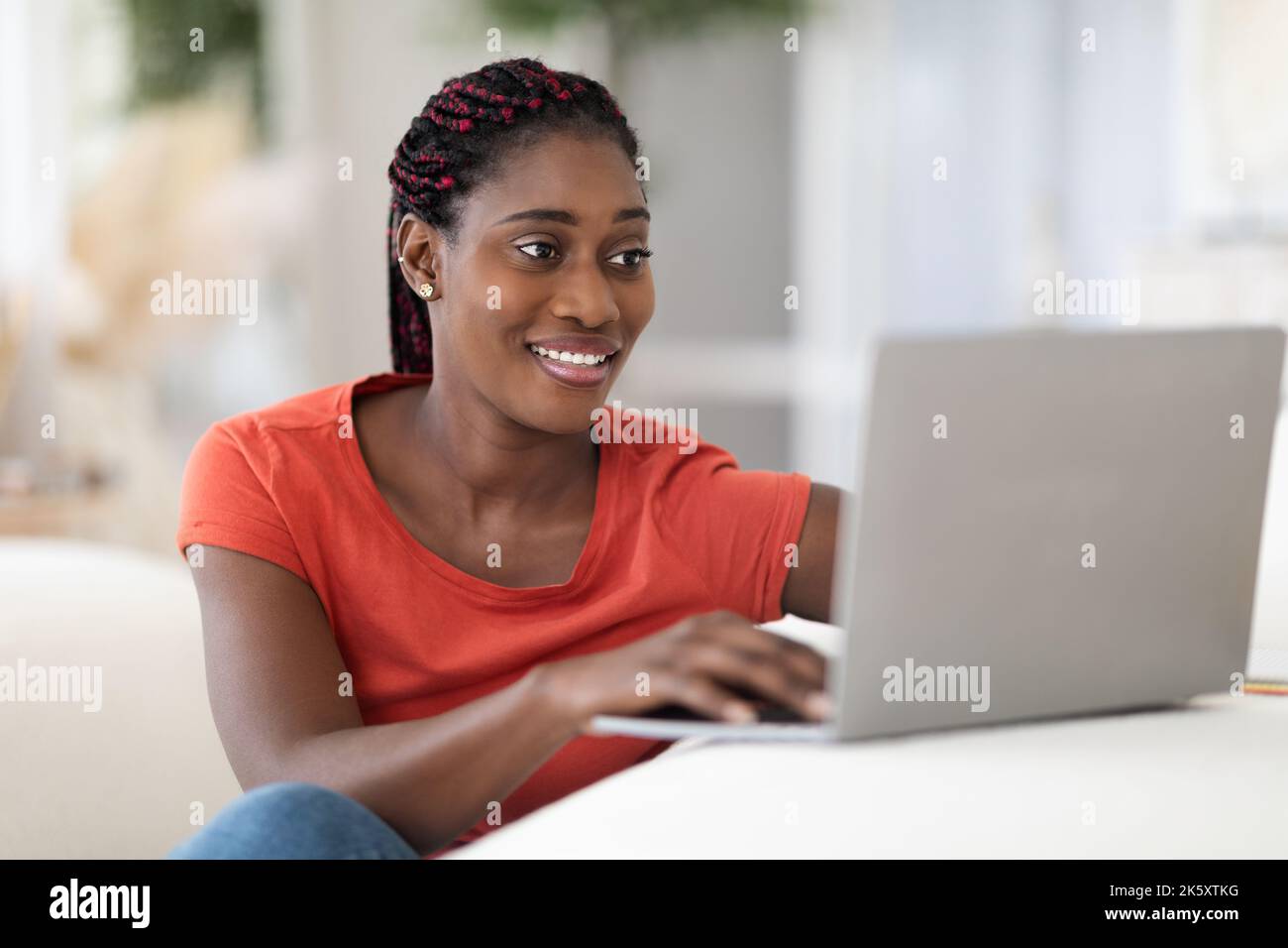 Beautiful Young Black Woman Using Laptop While Sitting At Desk At Home Stock Photo